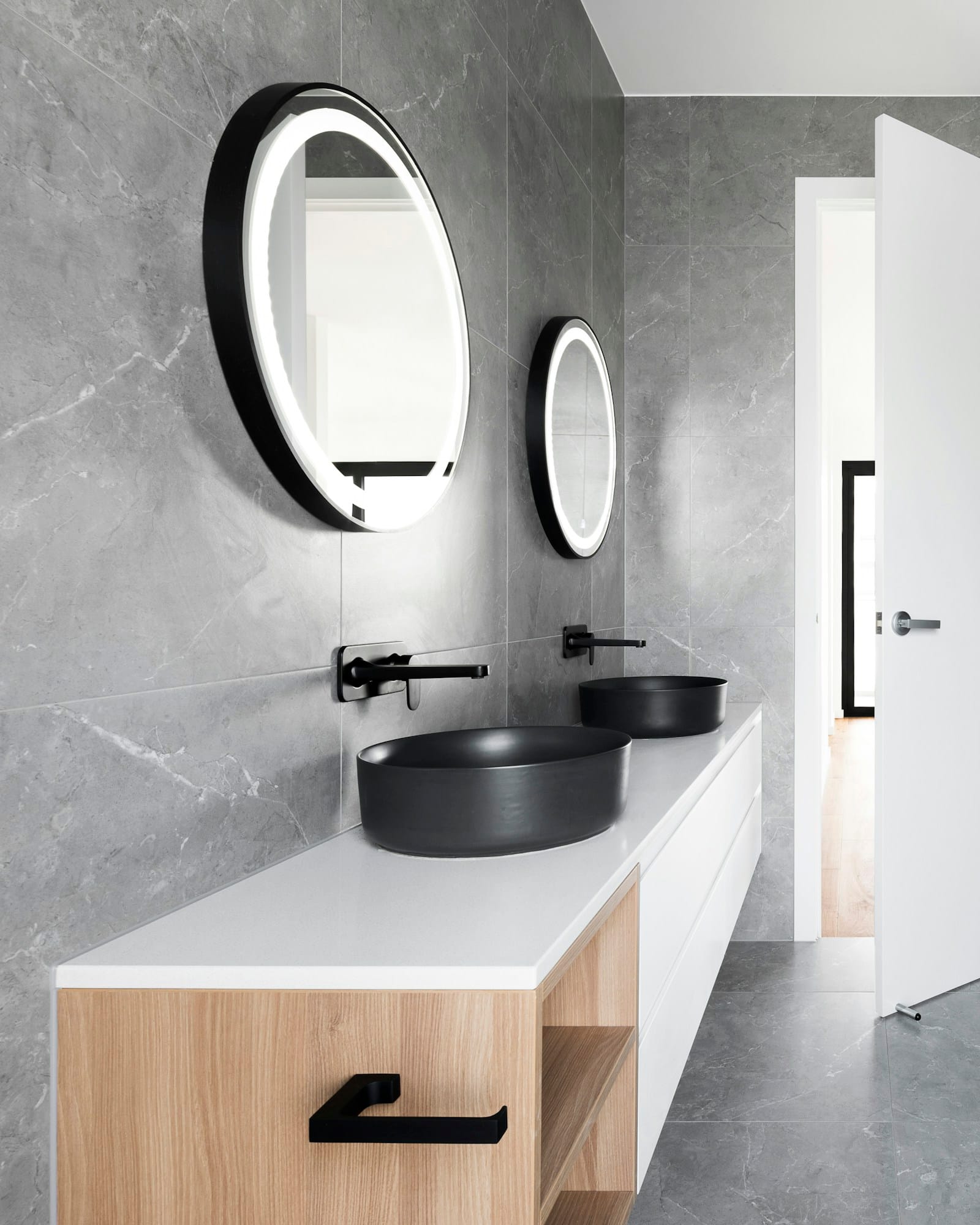 A bathroom in polished concrete with twin oval mirrors and a freestanding bath